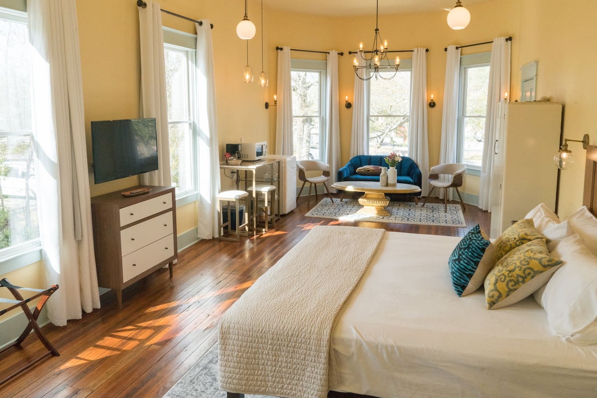 A bedroom with a large bed, a desk, a television, and a seating area with a sofa and chairs.