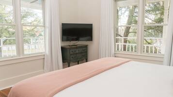 A bedroom with a bed, a dresser, a TV, and large windows with curtains.