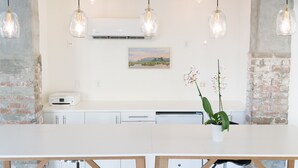 Een moderne keuken met een wit aanrecht, hangende lampen, een bakstenen muur en een schilderij.