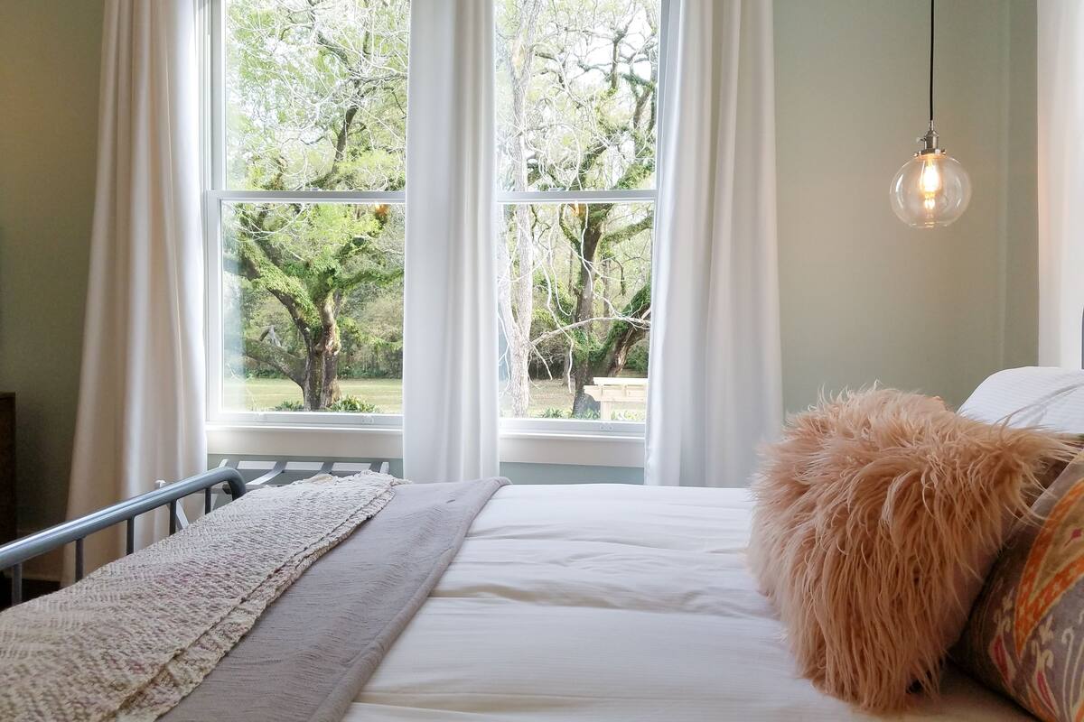 A bedroom with a bed, a window with curtains, and a hanging light fixture.