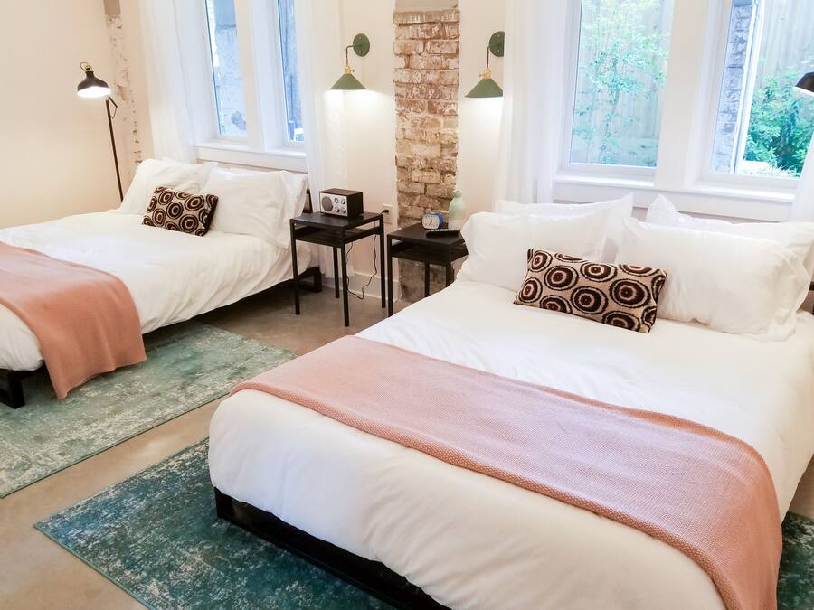 A hotel room with two beds, a brick wall, and a window with a view of greenery.