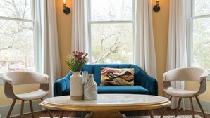 Een kamer met een blauwe bank, twee witte stoelen, een ronde tafel en een kamerbreed tapijt met een patroon.