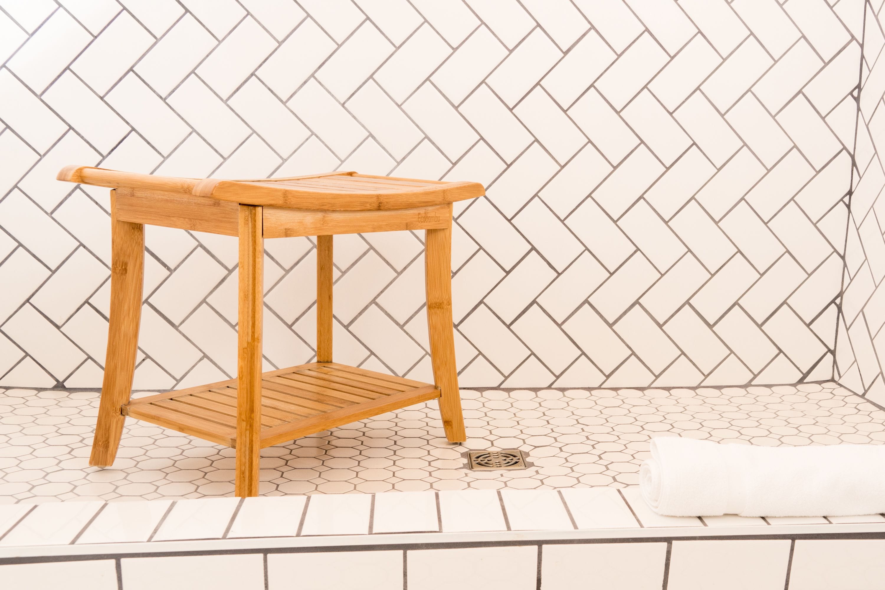 Un taburete de madera con asiento tejido y un estante, sobre un piso de baldosas con patrón de espiga.