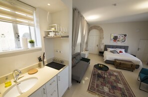 A modern hotel room with a kitchen area, a sofa, a bed, and a small table. - Mamilla Design Apartments (Jerusalem)