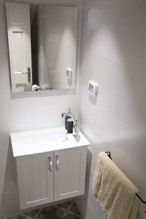 A bathroom with a white sink, a mirror above it, a towel hanging on a rack, and a toilet paper holder on the wall. - Mamilla Design Apartments (Jerusalem)