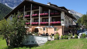 A hotel with multiple balconies adorned with flowers, outdoor seating, and a mountain backdrop. - Alpina Mountain Resort (Stelvio)