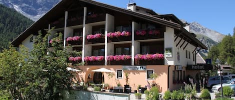 Un hotel con varios balcones decorados con flores, mobiliario exterior y el paisaje de montañas al fondo.