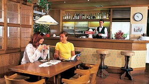A bar area with wooden furniture, a bar counter, and a clock on the wall. - Alpina Mountain Resort (Stelvio)