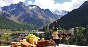 A scenic mountain view with a table featuring a bottle of wine, glasses, cheese, and bread. - Alpina Mountain Resort (Stelvio)