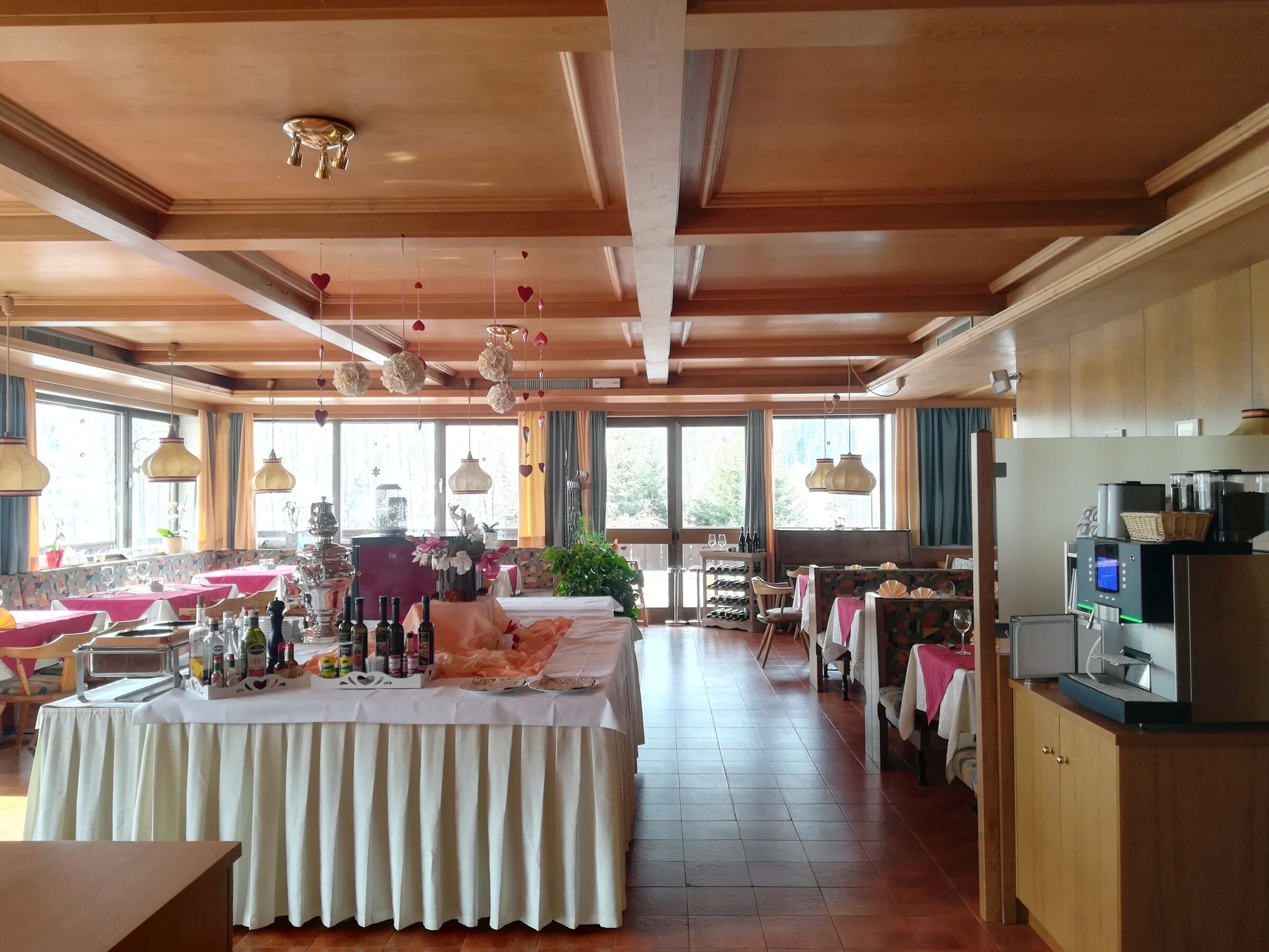 Ein geräumiger Hotel-Speisesaal mit mehreren Tischen, einer Küchenzeile inklusive Geräte und großen Fenstern für natürliches Licht.
