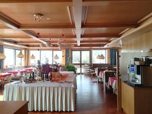 A spacious hotel dining area with multiple tables, a kitchen area with appliances, and large windows providing natural light. - Alpina Mountain Resort (Stelvio)
