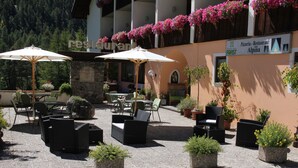 An outdoor patio area with tables and chairs, surrounded by potted plants and flowers. - Alpina Mountain Resort (Stelvio)