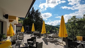 Een terras buiten met gele parasols, rieten meubels en uitzicht op de bergen.
