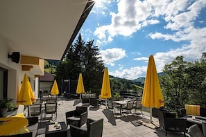 An outdoor patio with yellow umbrellas, wicker furniture, and a view of the mountains. - Erika (Wagrain)
