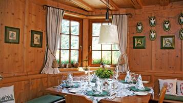 A wooden dining room with a table set for four, large windows, and wall-mounted animal skull decorations.
