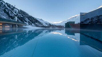 A clear pool with a mountain backdrop, a bridge, and a building with a sloped roof.