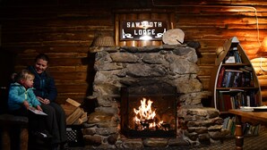 Una habitación acogedora con chimenea de piedra, una estantería y un letrero que dice "Sawtooth Lodge".
