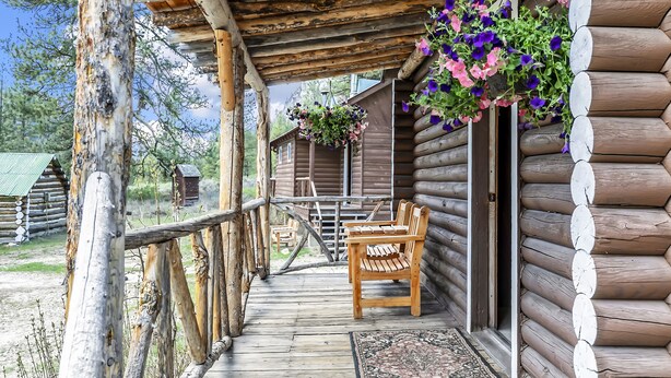 Una cabaña de madera con porche, bancos de madera y cestas de flores colgantes.