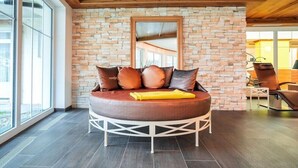A modern room with a stone wall, a round bed with brown cushions, and a yellow throw blanket. - Wellnesshotel Schonruh - Adults Only (Seefeld in Tirol)