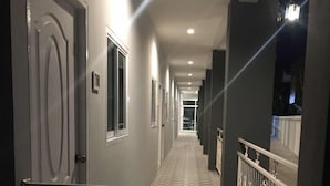 Een lange, smalle gang met een geruit vloerkleed, die uitkomt op een balkon met een leuning.