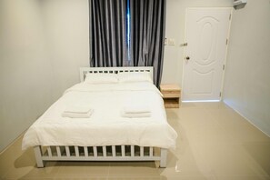 A neatly made bed with white bedding and two towels, a wooden nightstand, a door, and a tiled floor. - Lullaby Residence by Smarnbook (Phayakkhaphum Phisai)