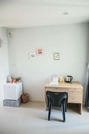 Una habitación pequeña y ordenada con un escritorio de madera, una silla negra, un refrigerador blanco y algunos objetos personales en la pared.