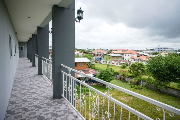 A balcony with a checkered floor, white railing, and a view of a residential area with houses and greenery. - Lullaby Residence by Smarnbook (Phayakkhaphum Phisai)