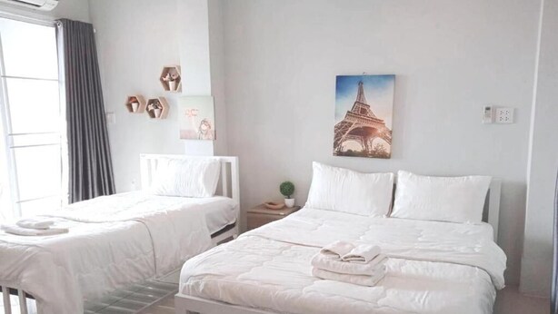 Hotelkamer met twee bedden, een groot raam met gordijnen, een wandairconditioner en een afbeelding van de Eiffeltoren.