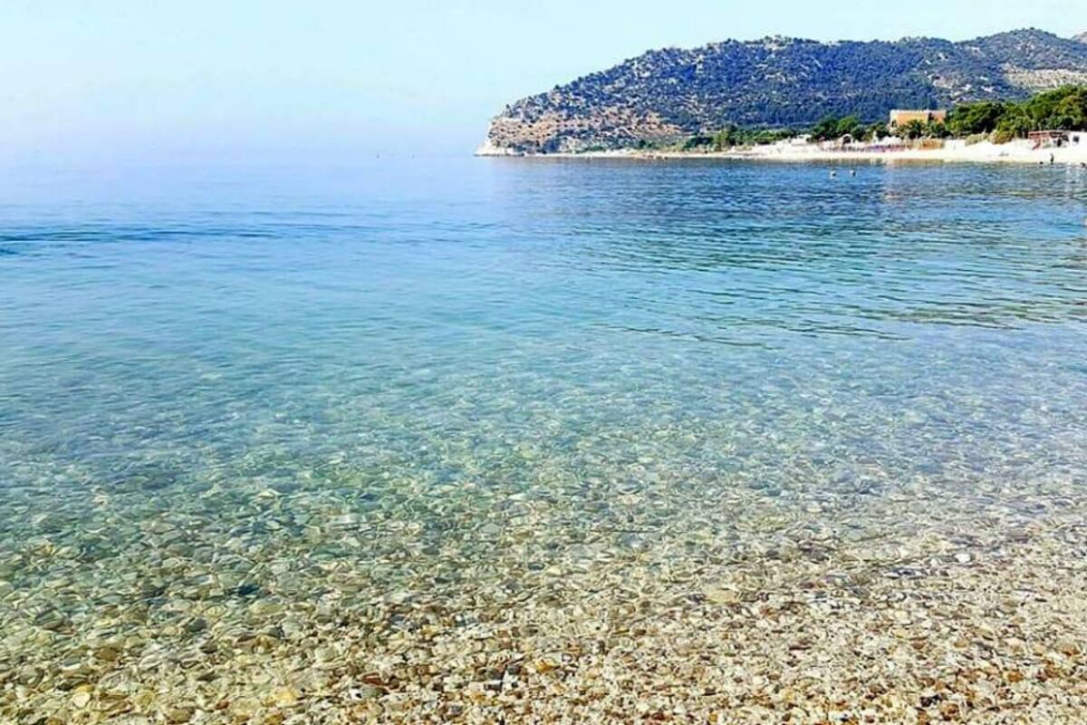 Una playa despejada con piedras visibles y una colina distante con edificios.