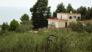 Una casa de dos pisos con balcón, rodeada de vegetación y vista al agua.