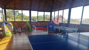 Amplia zona de juegos interior con mesa de fútbol de mesa, mesa de ping pong y diversas estructuras de juego.