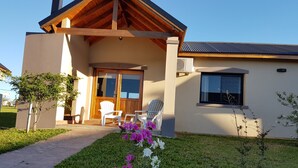 Una casa moderna con un porche de madera, un ventanal corredero y un pequeño jardín con flores.
