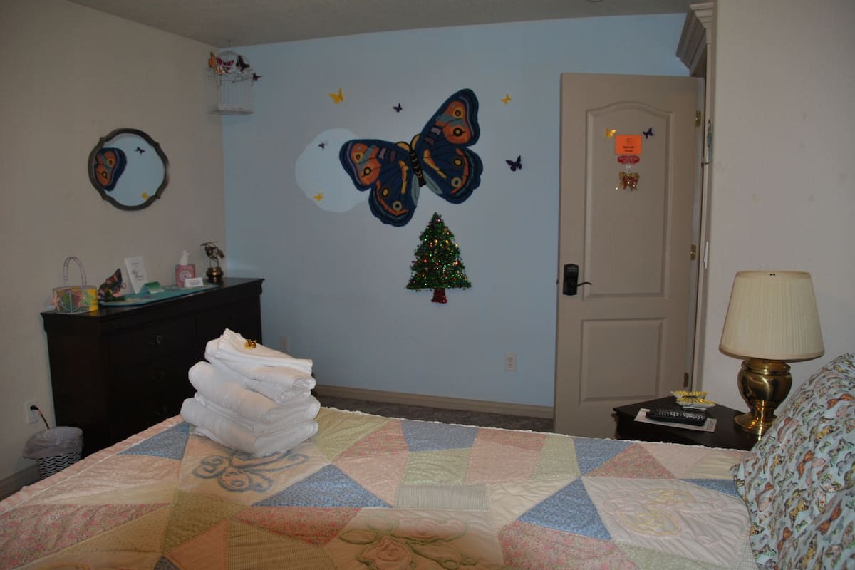 A bedroom with a bed, a dresser, a Christmas tree, and butterfly wall art.