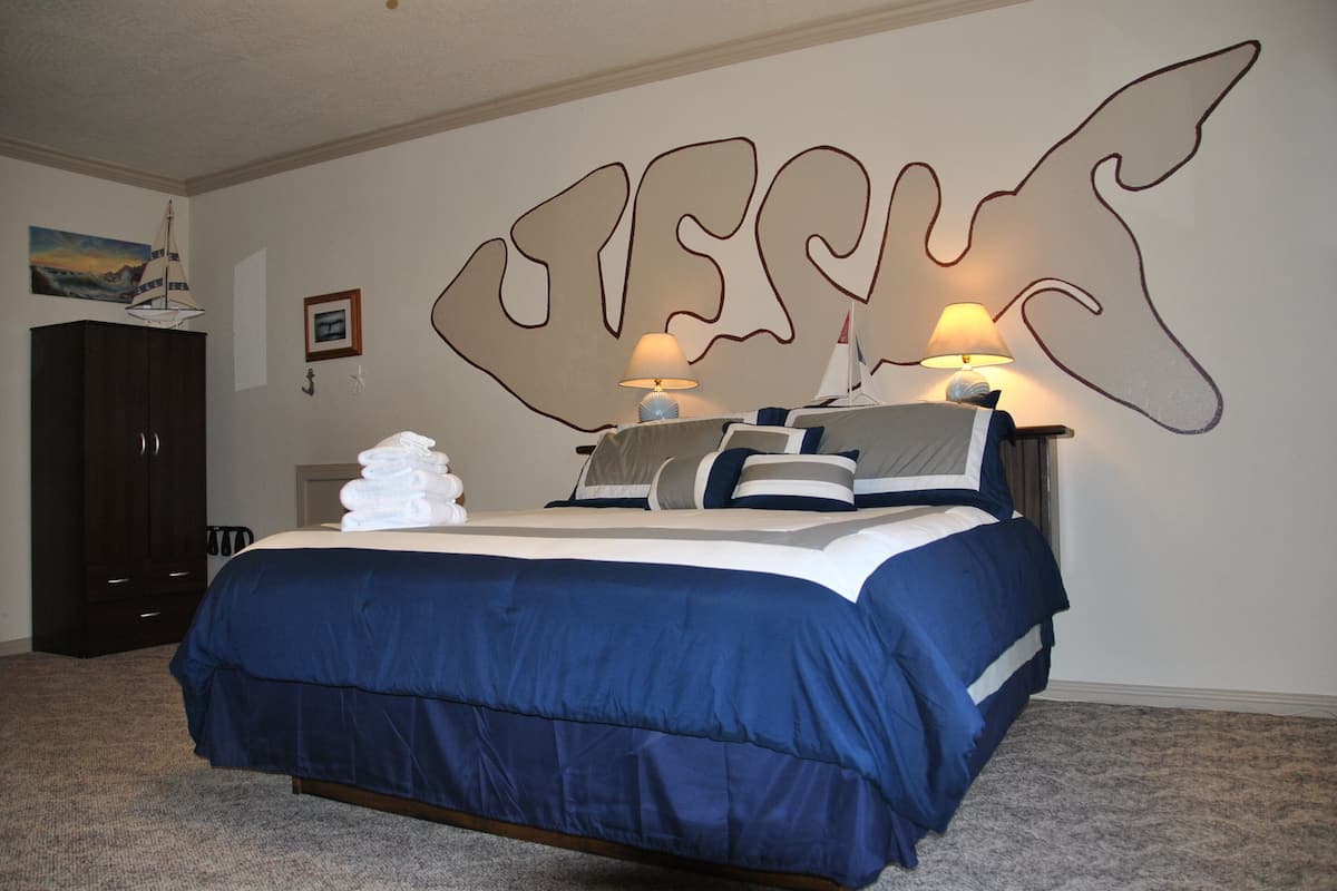 A bedroom with a large bed, dark wooden wardrobe, and a wall with a large abstract design.