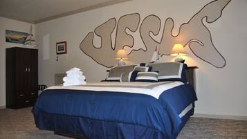 A bedroom with a large bed, dark wooden wardrobe, and a wall with a large abstract design.