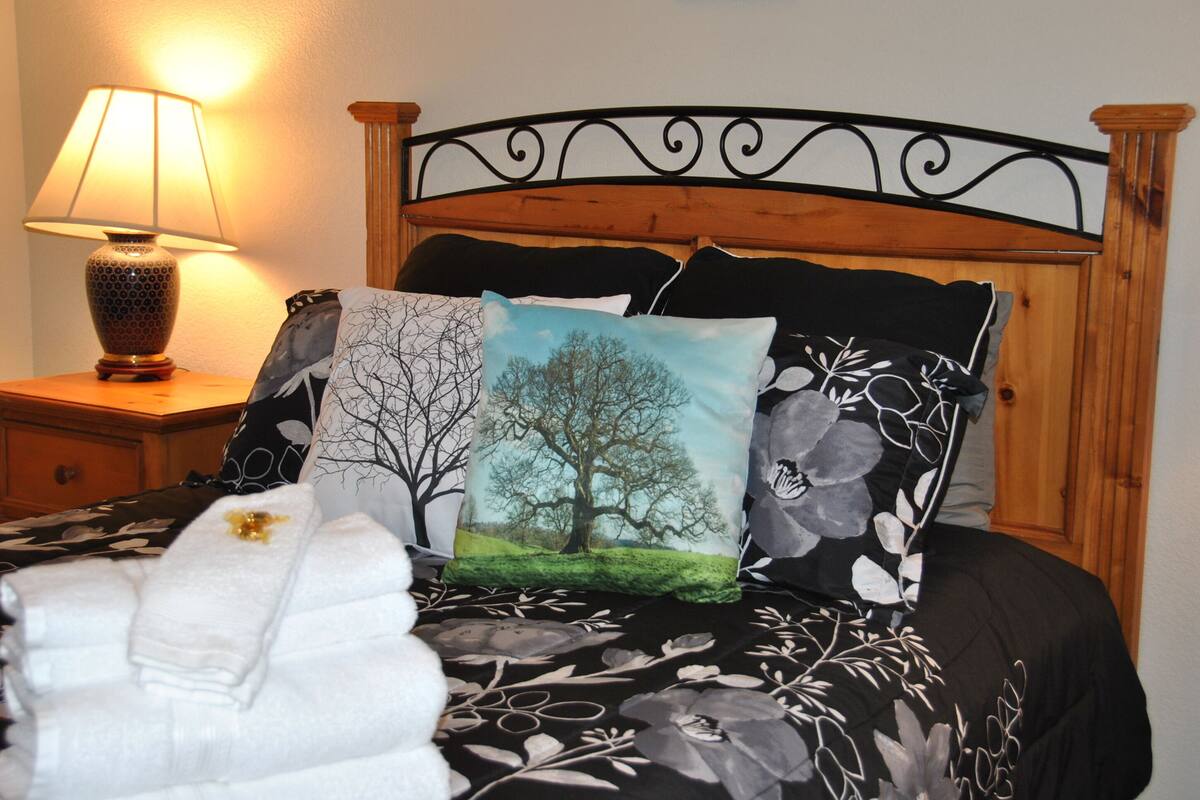 A neatly made bed with a floral bedspread, a wooden headboard, and a nightstand with a lamp.