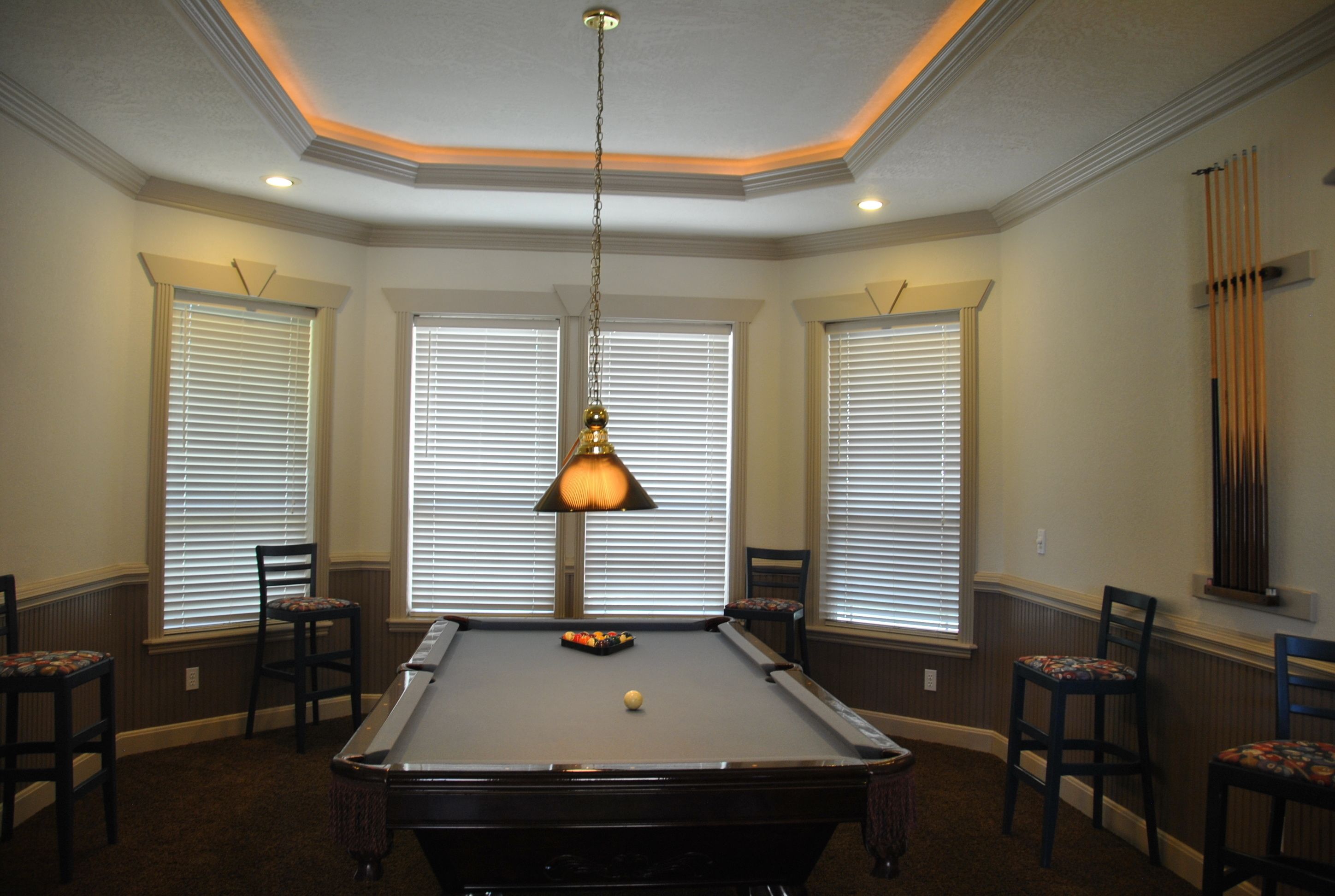 A pool table in a room with three windows, chairs, and a hanging lamp.