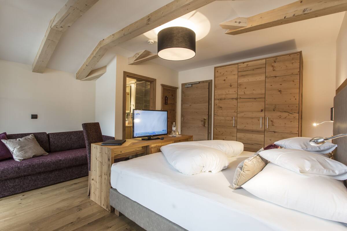 A bedroom with a bed, a wooden wardrobe, a television on a wooden table, and a purple sofa.
