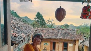 Una persona seduta su una panchina di legno con vista su edifici tradizionali e un paesaggio montuoso.