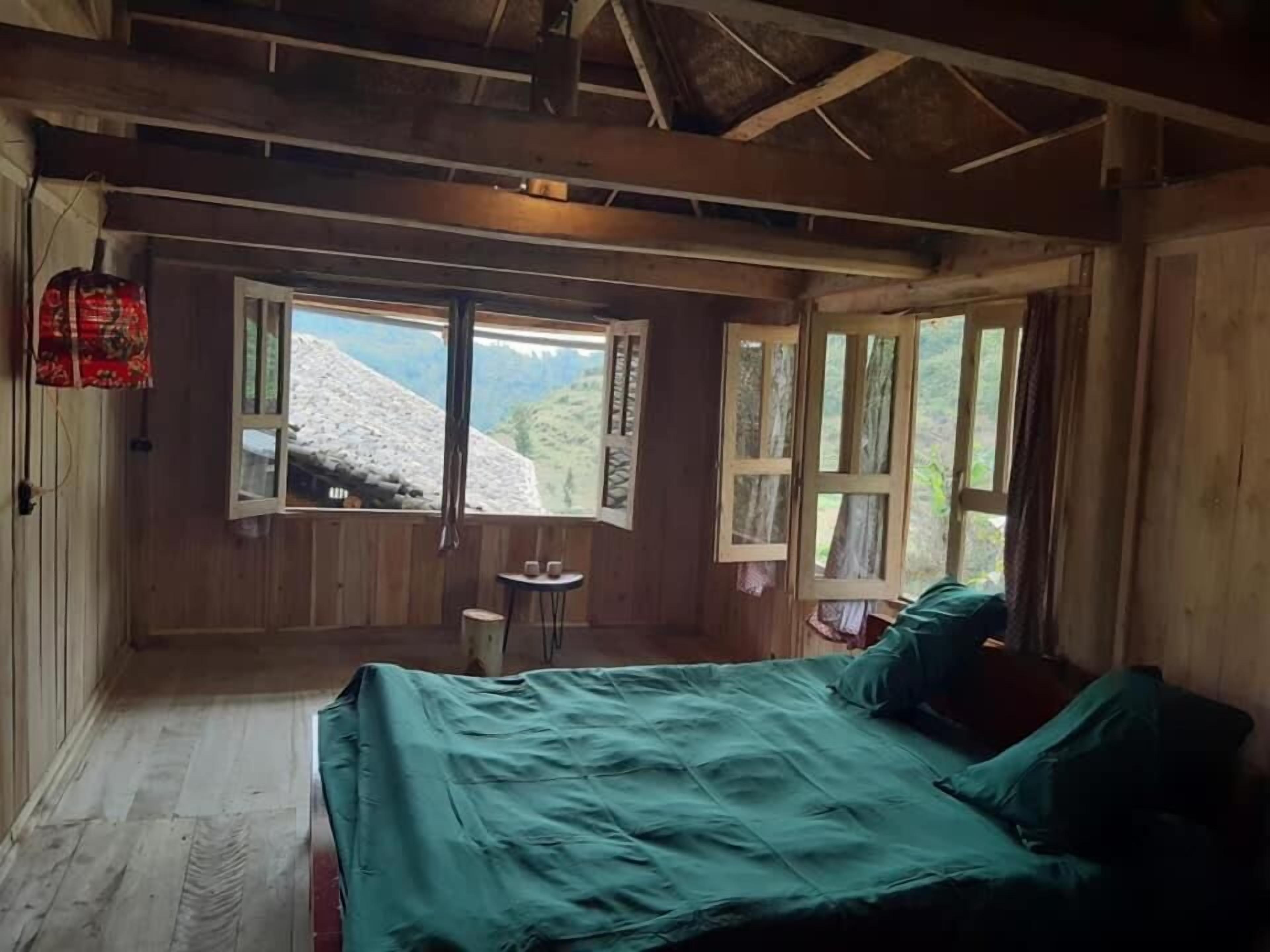 Habitación tipo cabaña de madera con una cama, una mesita y un ventanal con vistas a montañas nevadas.