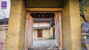 Un corridoio rustico con pavimento in pietra, travi in legno e una porta in legno tradizionale alla fine.