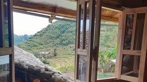 Una stanza in legno con un'ampia finestra aperta, un piccolo tavolo rotondo con due tazze e uno sgabello di legno rustico.