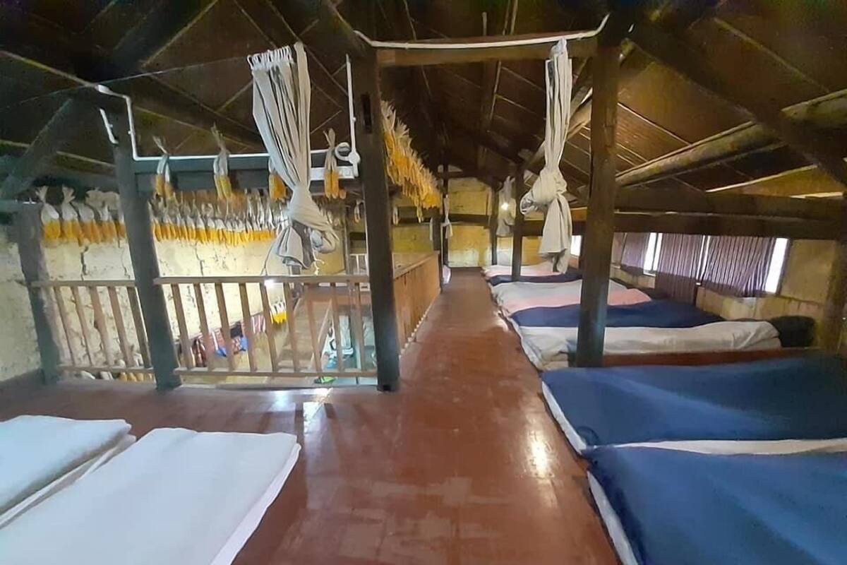 A hostel room with bunk beds, a wooden floor, and a balcony with yellow decorations.