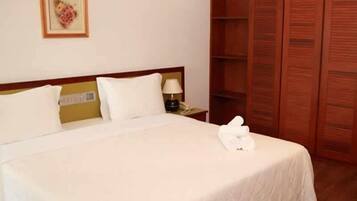 Uma cama bem arrumada com roupa de cama branca, um abajur e um pequeno quadro na parede.