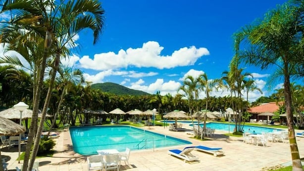 Un área de piscina en un resort, con varias piscinas, sillones de descanso, sombrillas y palmeras.