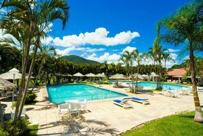 Un espace piscine d’un complexe hôtelier comprenant plusieurs piscines, des chaises longues, des parasols et des palmiers.