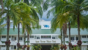 El exterior del Hotel Palacio Agua Morna, con techo verde, rodeado de palmeras y un jardín bien cuidado.