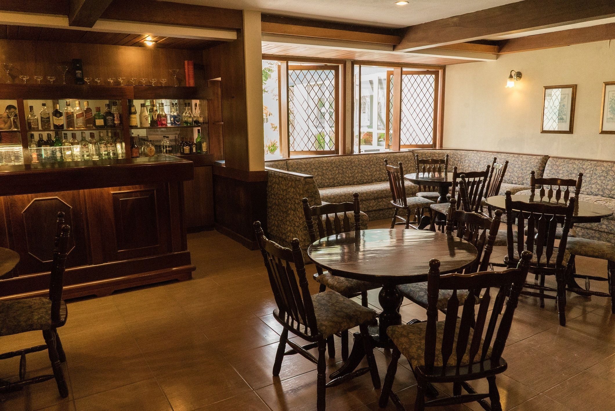 A bar area with wooden furniture and a variety of liquor bottles. There are multiple seating areas with tables and chairs.