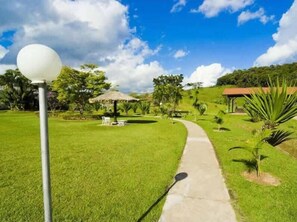 Un sendero que atraviesa un jardín cuidado, con un paraguas de paja y un poste de luz blanco y esférico.