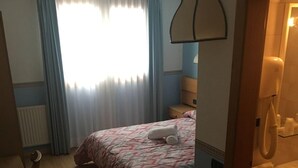 Una habitación de hotel con cama, sillón, escritorio, teléfono y baño.